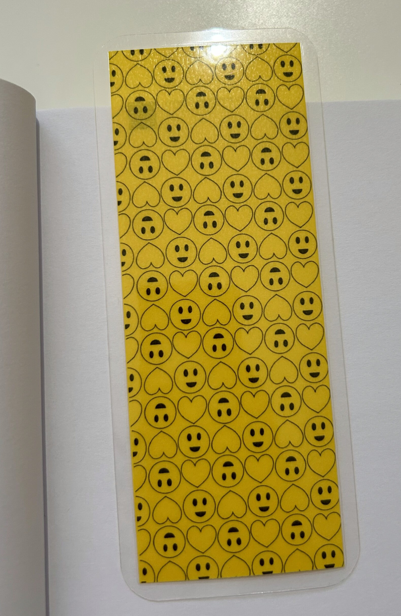 Handgemaakte gelamineerde gele boekenlegger met smileys en hartjes liggend op een boek