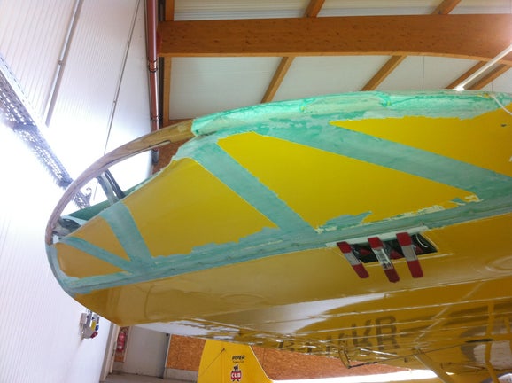 Close-up of a damaged yellow Piper Super Cub wing inside a hangar, patched and clamped after a botched bush pilot attempt by Marcel Romdane. From Riches to Rags: An African Odyssey – Campfire Syndicate LLC.