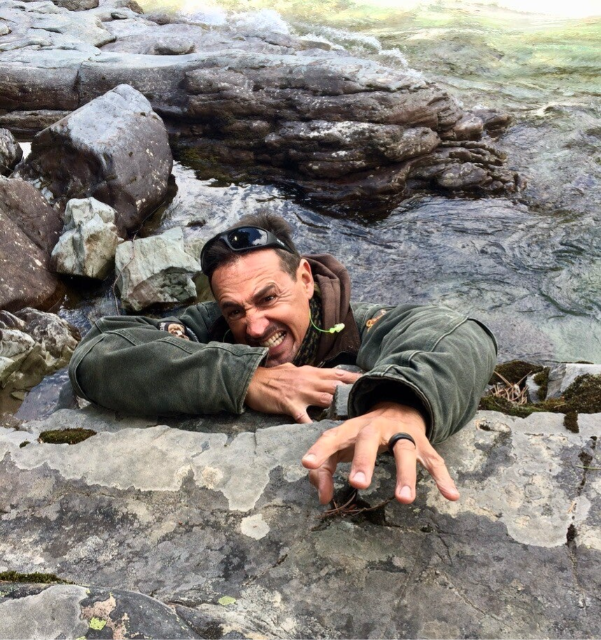 Marcel Romdane, co-founder of Campfire Syndicate LLC, clinging to a cliff edge with trademark desperation and grin — the human embodiment of inbox overwhelm and startup stress.