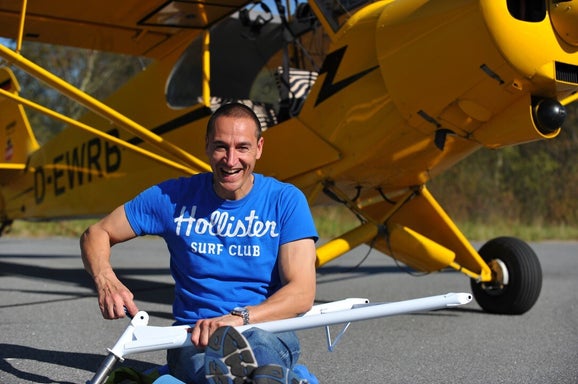 Marcel Romdane sits laughing in front of his yellow Super Cub airplane while assembling parts. Campfire Syndicate LLC. From Riches to Rags: An African Odyssey, Part XI – Grease, Grit and the Gospel According to Kalli.