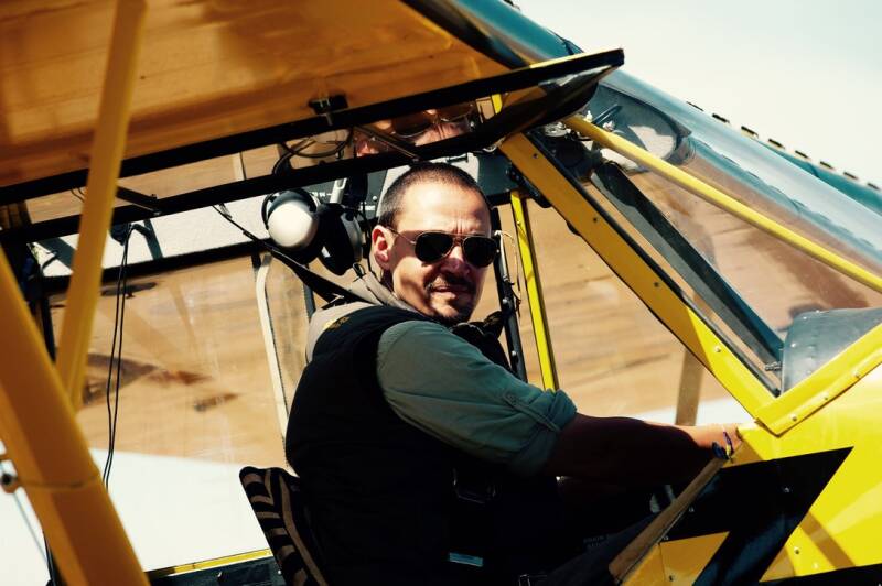 Marcel Romdane in cockpit of yellow Super Cub during true story disaster memoir. Scene from audiobook What Could Possibly Go Wrong? — bush pilot, aviation chaos, Kenya survival, dark humor, near-death flying, narrated by author himself.
