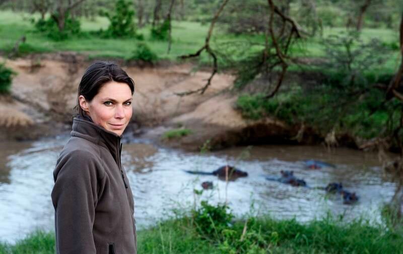  Nicole Romdane during a Kenya safari, rethinking life choices while hippos lurk behind her. A scene from What Could Possibly Go Wrong? — the original Romdane memoir of travel disasters, bush pilot delusions, and marital misadventures.