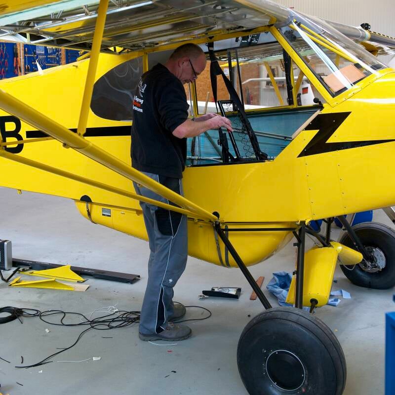 Aviation mechanic working on yellow Super Cub aircraft inside hangar. Marcel Romdane’s Campfire Syndicate LLC project begins here. From Riches to Rags: An African Odyssey, Part XI – Grease, Grit and the Gospel According to Kalli.