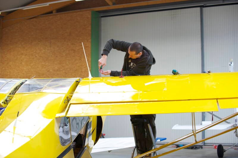 Marcel Romdane attempting Super Cub aircraft repairs in hangar, pretending to be a mechanic before Africa deployment – Germany, 2011.