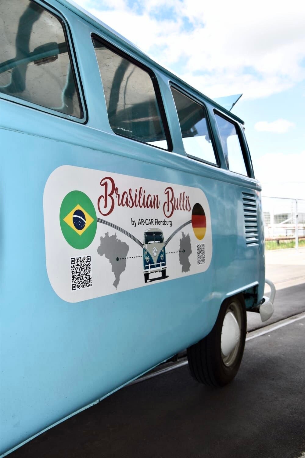 Side view of a blue VW T1 Brazilian Bulli with Brazil–Germany flags, QR code, and map graphics — symbol of Romdane’s van import dream turned Flensburg ghosting fiasco, leaving him oil-soaked and abandoned in the Wyoming dirt.