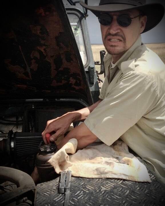 Man working angrily under the hood of a broken Land Rover near Westgate Mall in Nairobi. Close-up image tied to Marcel Romdane’s story in What Could Possibly Go Wrong? about repeated Land Rover failures and British engineering misery.