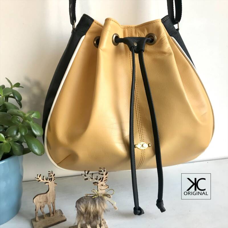 Zachtgele schoudertas met zwarte zijkanten en witte accenten, zomerse crossbody in zachtgeel, zwart en wit, leren tas met trekkoord