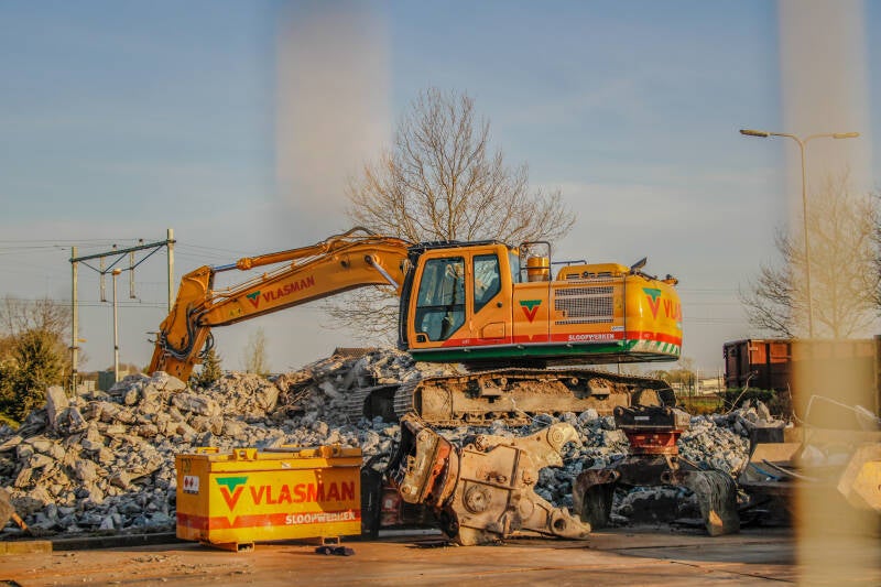 Een kraan is bezig met het slopen van een oud pand.