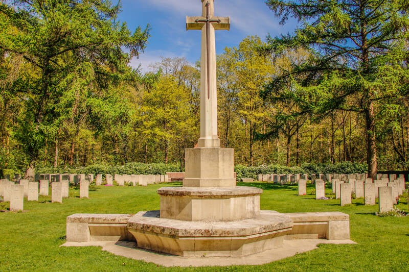 Kruis in het midden van een bos met daar om heen graven van soldaten.