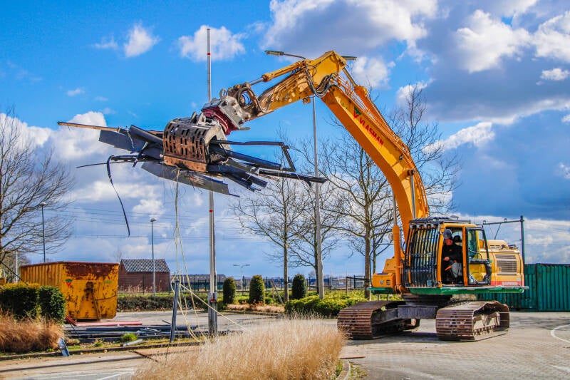 Een graafmachine is bezig met het verzamelen van metalen onderdelen.