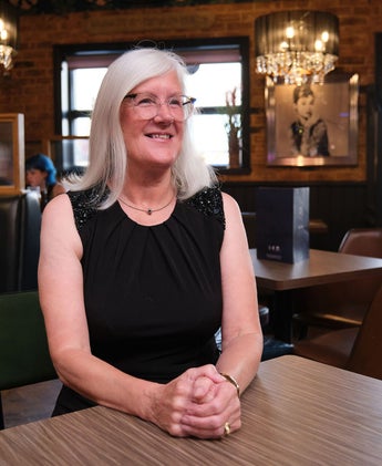 Elegant woman with long white hair and black sleeveless dress seated in elegant Whitby bar with chandeliers and rustic decor, evoking a luxury bar where you can be served chocolate cocktails