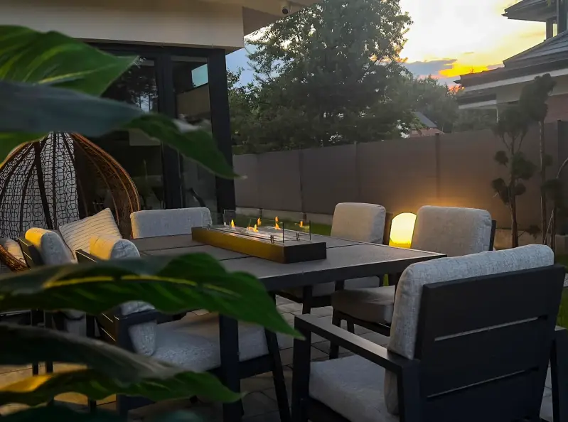 Bio-ethanol haard van 1200 mm op een donkere buitentafel bij zonsondergang, met lounge stoelen en planten in een moderne tuinomgeving