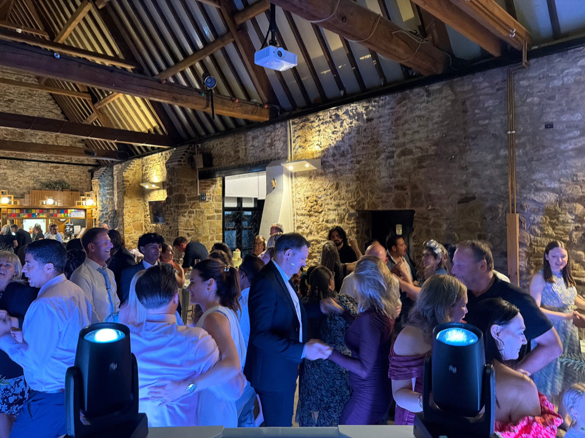 Wedding guests filling the dancefloor beneath exposed timber beams in a stone barn