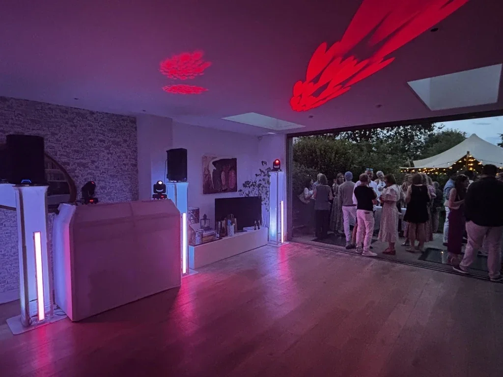 White MHX DJ booth and lighting at a private house party, with guests in the garden beyond the open doors
