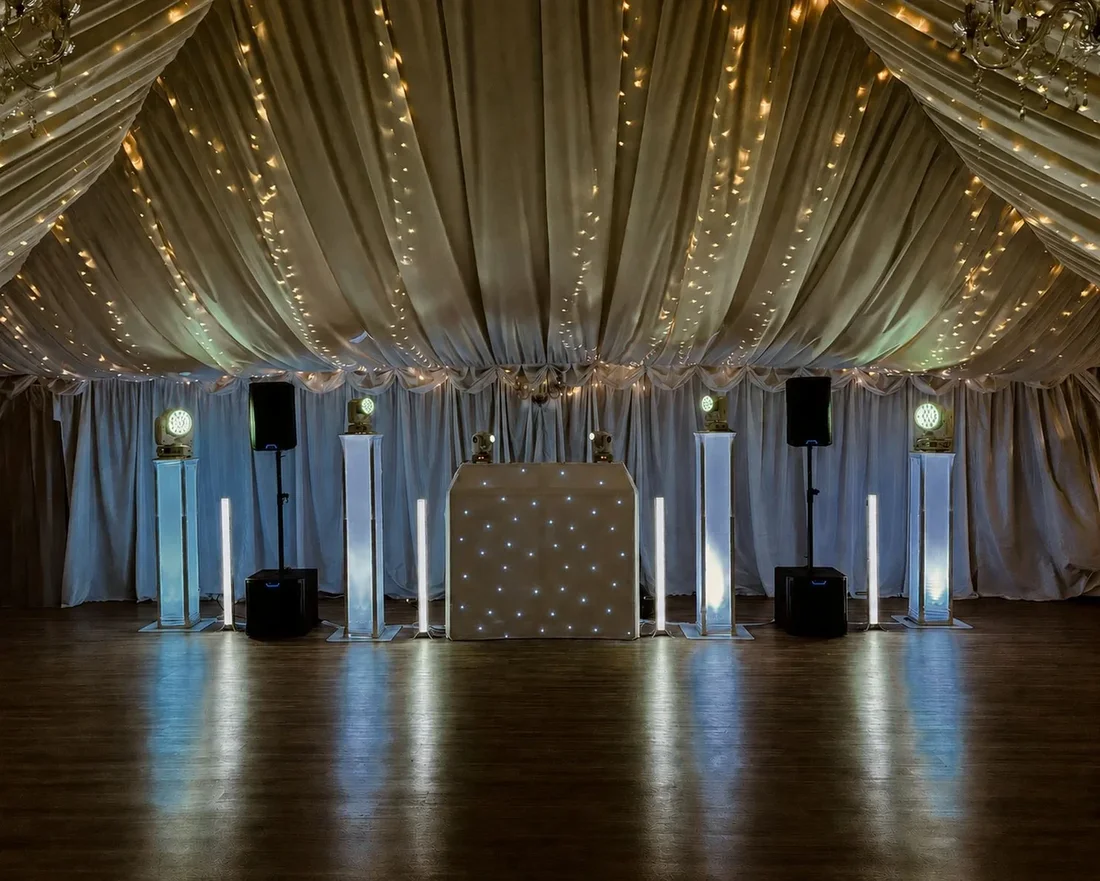 MHX white wedding DJ setup beneath a warmly lit draped ceiling