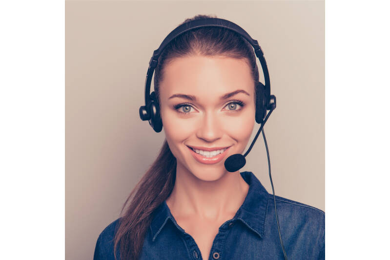 Woman wearing headset with microphone, denim shirt, neutral background.