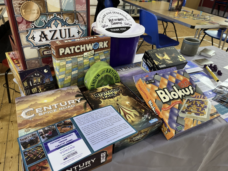 Selection of board games on a table, including Patchwork, Azul, Mysterium Park and Blokus. There is also a donation bin at the back of the table.