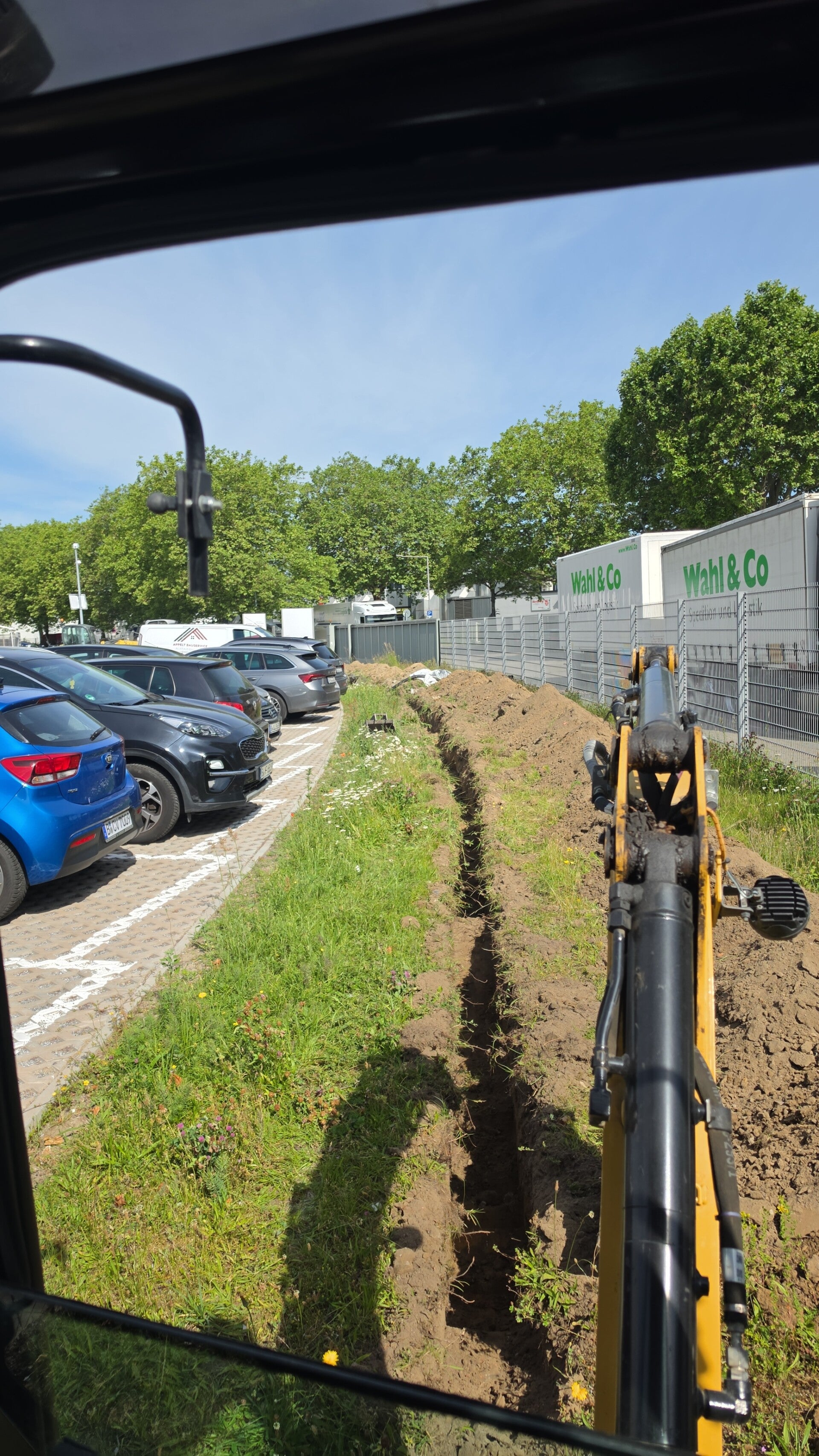 Blick aus einer Baggerkabine auf einen schmalen Graben neben einer Parkplatzfläche
