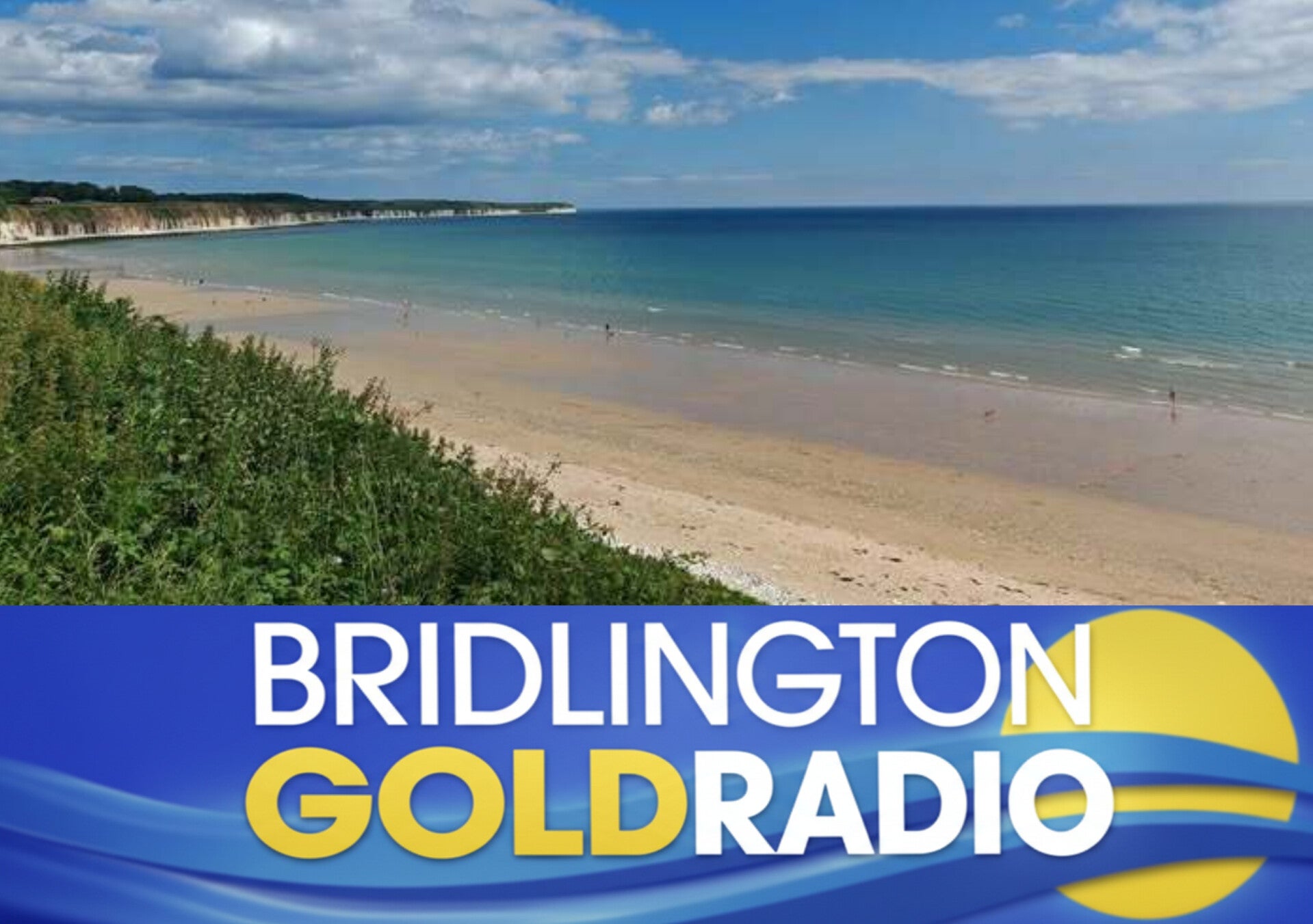 A scenic view of Bridlington’s coastline showing golden sand, calm turquoise sea, and white cliffs under a bright blue sky with scattered clouds. 