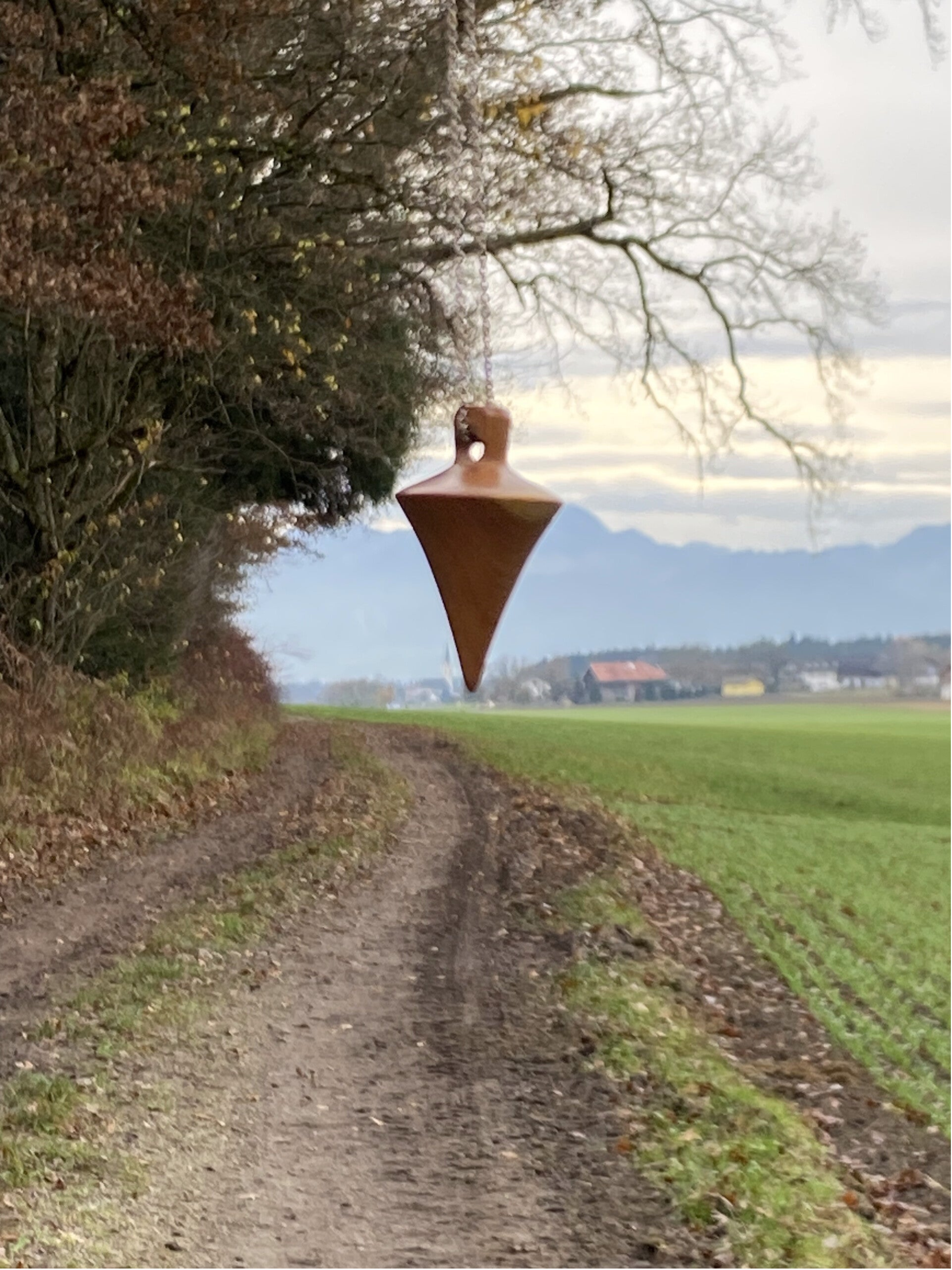 Geomantie in der Landschaft mit Pendel als radiästheschem Instrument. Vor Wald, Wiese und Bergen.  Es ist ein Hinweis auf Landschaftsgeomantie und das Wirken der Energien in der Natur.
