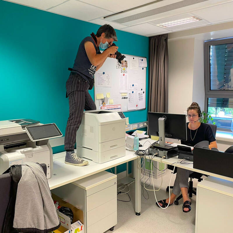 fotograaf Heidi Rombouts staat op een tafel en fotografeert een kantoormedewerker die aan een computer werkt