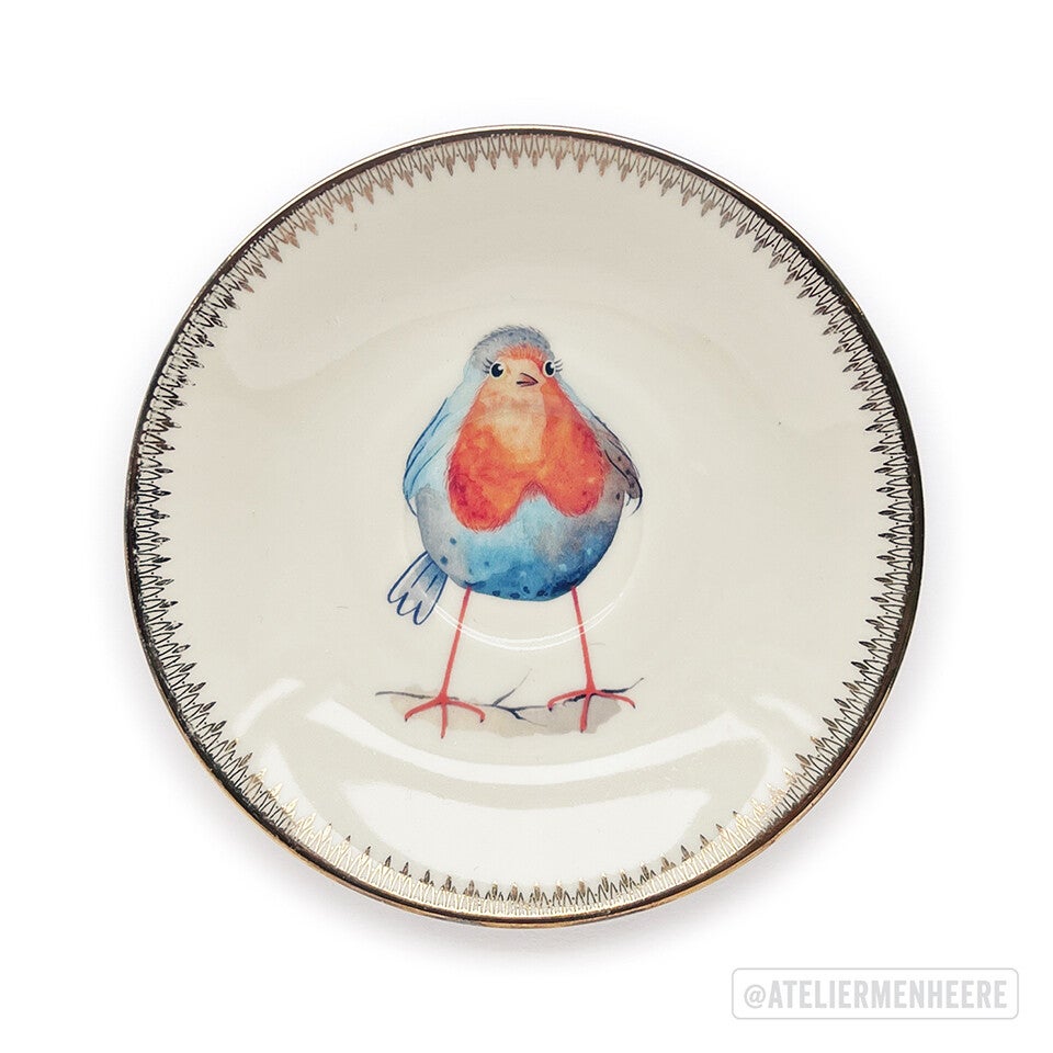 Klein porseleinen bordje mer de illustratie van een roodborstje. Dit is een decoratief bordje wat je aan de muur kunst hangen met een bordenhanger.