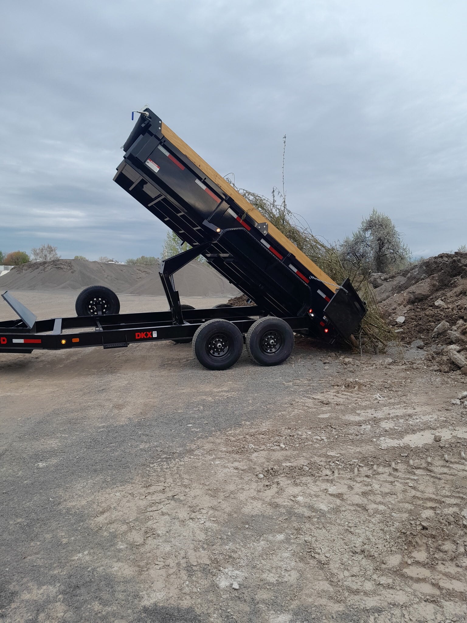 Junk removal 14 ft. hydraulic lift dump trailer with branches and debris dumping out