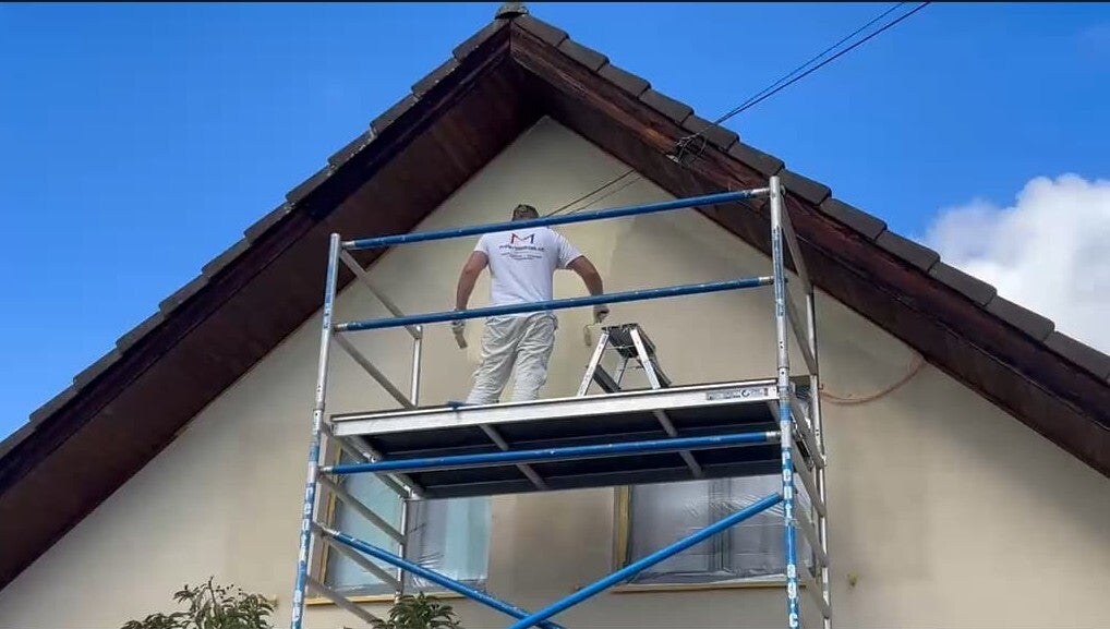 Maler Mathias bei professionellen Fassadenarbeiten an einer Giebelfassade auf einem Arbeitsgerüst.