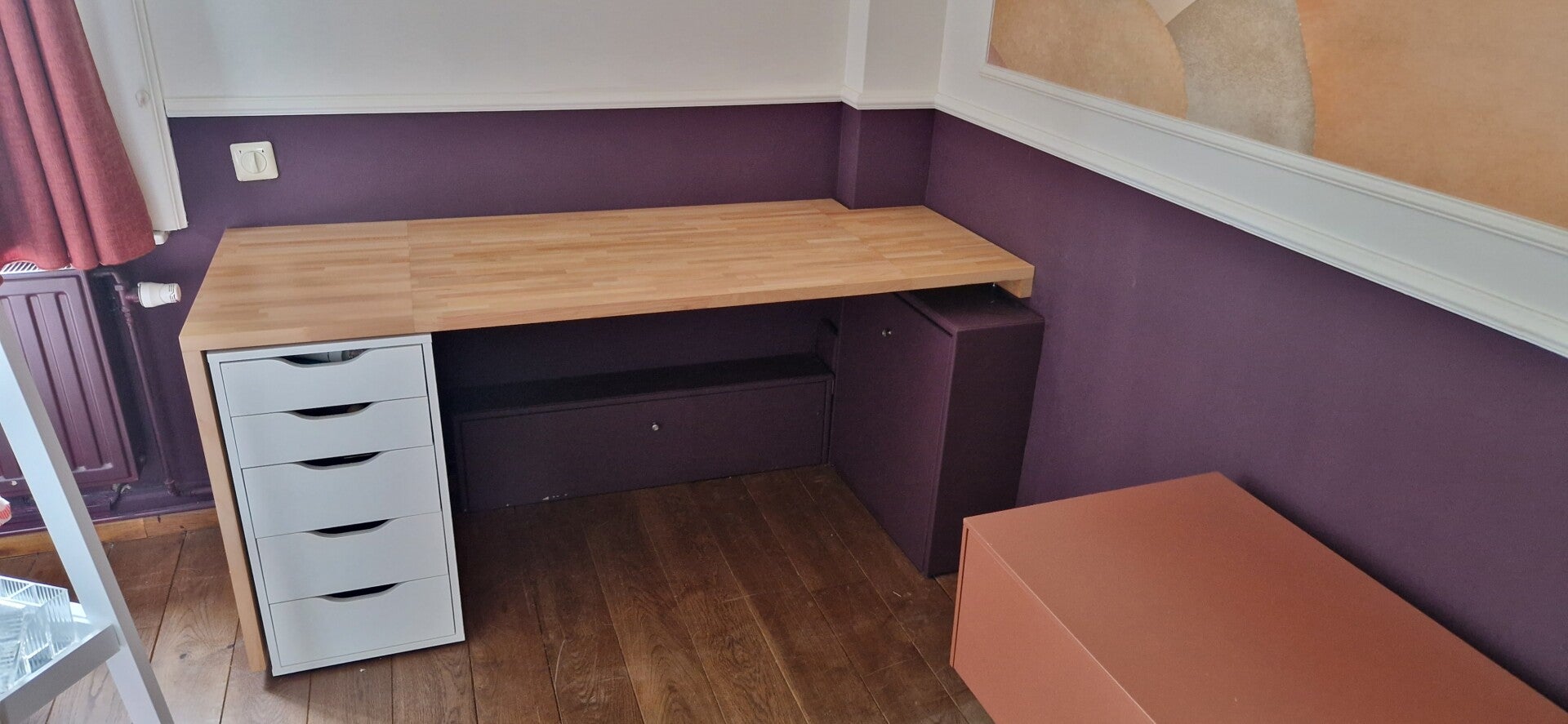 Bureau intégré sur mesure en bois, aménagé sous une fenêtre de toit dans une pièce aux murs violets.
