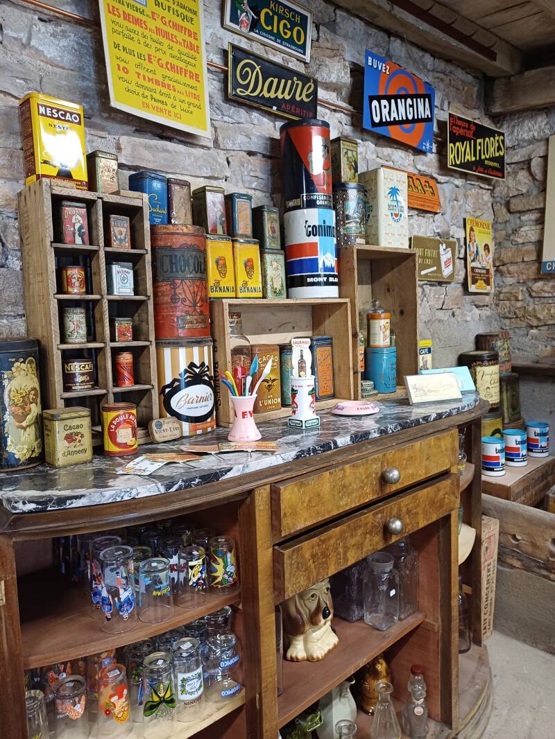 Des boîtes métalliques publicitaires de marque de chocolat avec, au mur, des cartons, tôles et plaques émaillées colorées