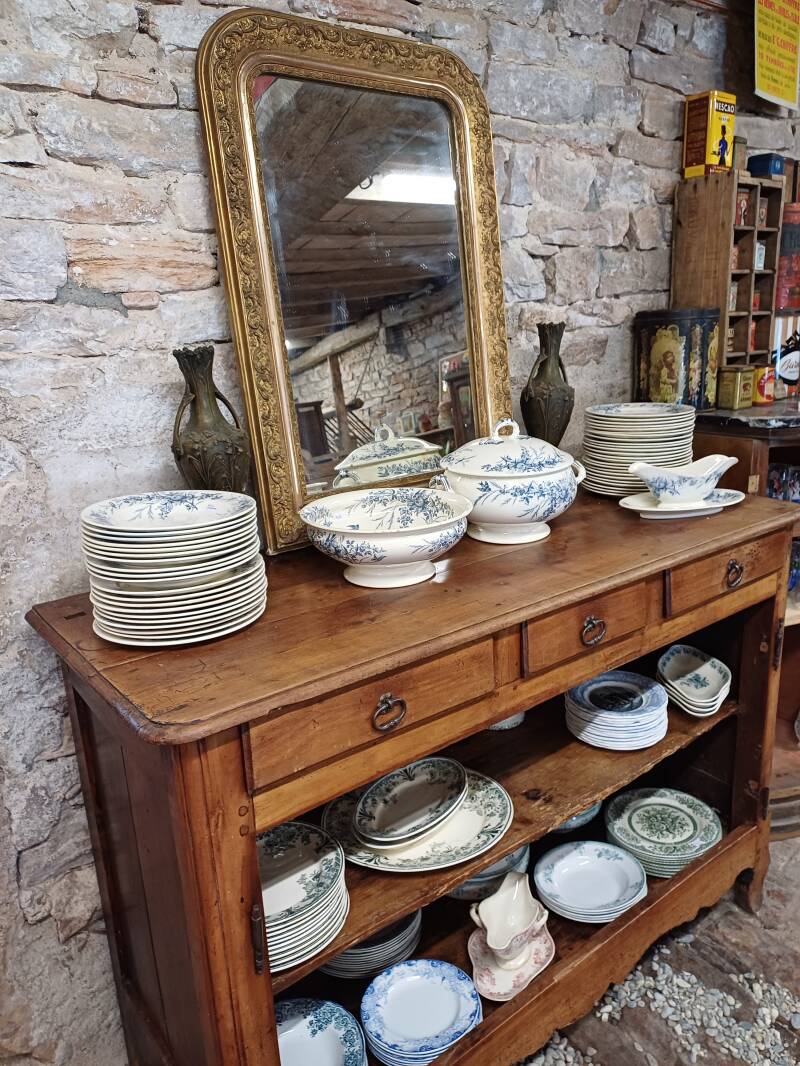 Vaisselle ancienne terre de fer présentée sur un buffet en bois devant un miroir ancien