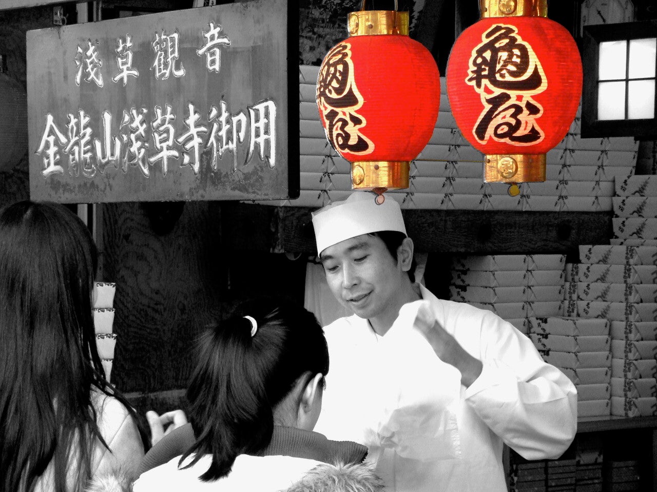 Japanse kok onder rode lampions verkoopt product aan twee vrouwelijke klanten