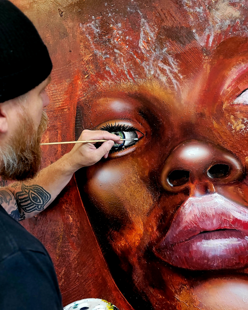 Willem Vos painting the eye of a large expressive portrait in his studio.