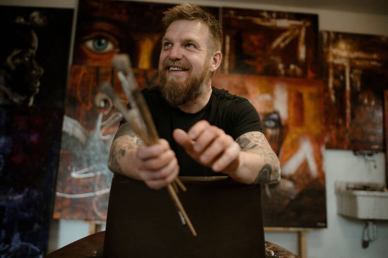Artist Willem Vos holding paintbrushes in his studio in Dwingeloo.