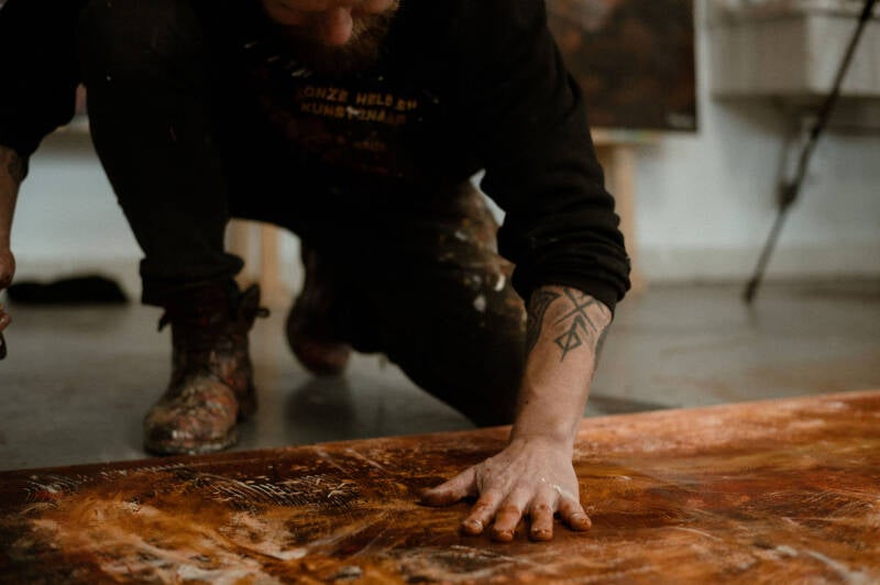 Willem Vos working paint by hand across a canvas on his studio floor.