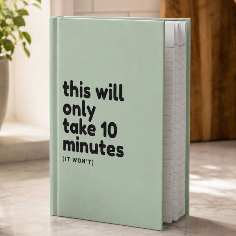 Sage green hardcover journal on hard surface with a plant in a window in the background.