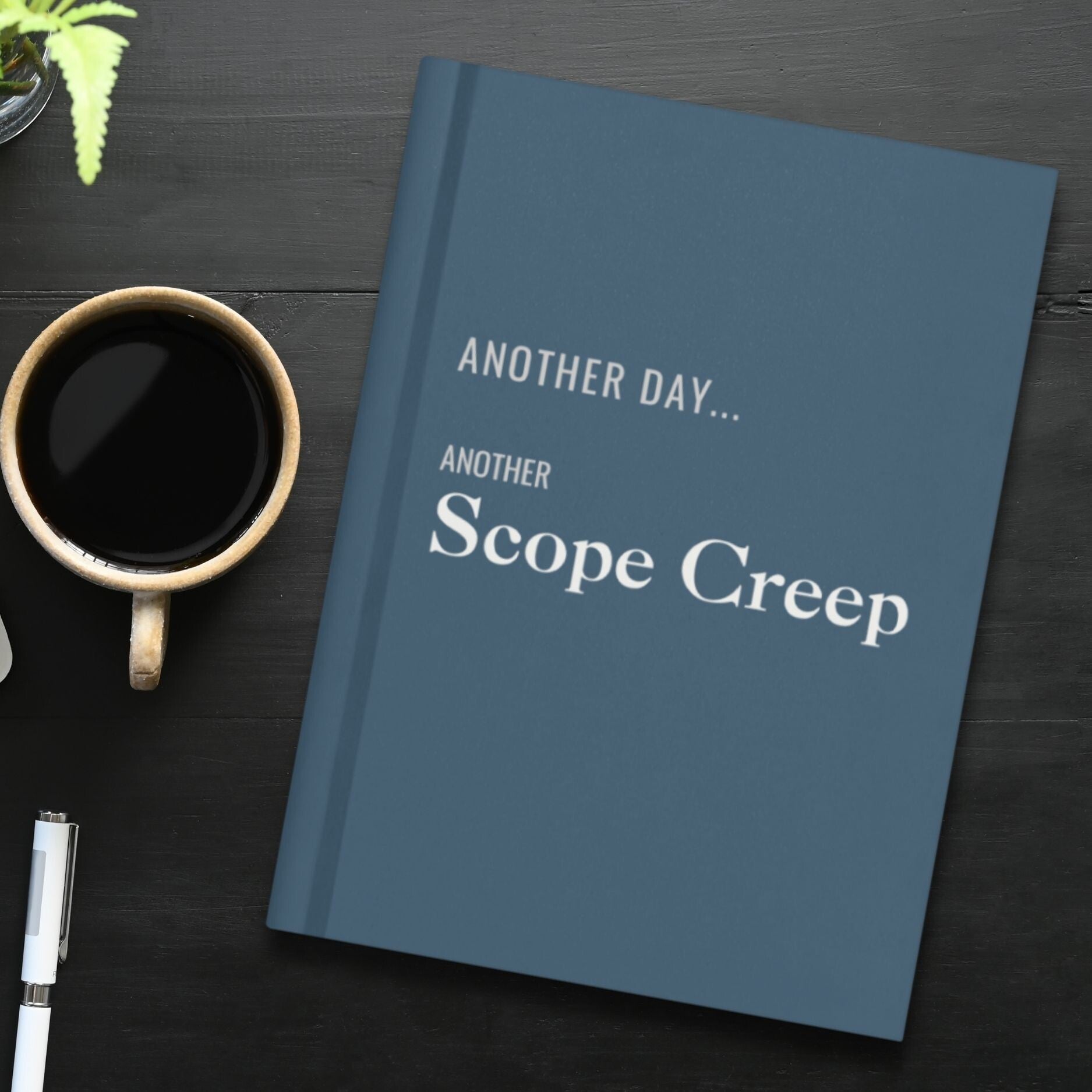 Slate blue hardcover journal titled Another Day...Another Scope Creep, resting on a desk.