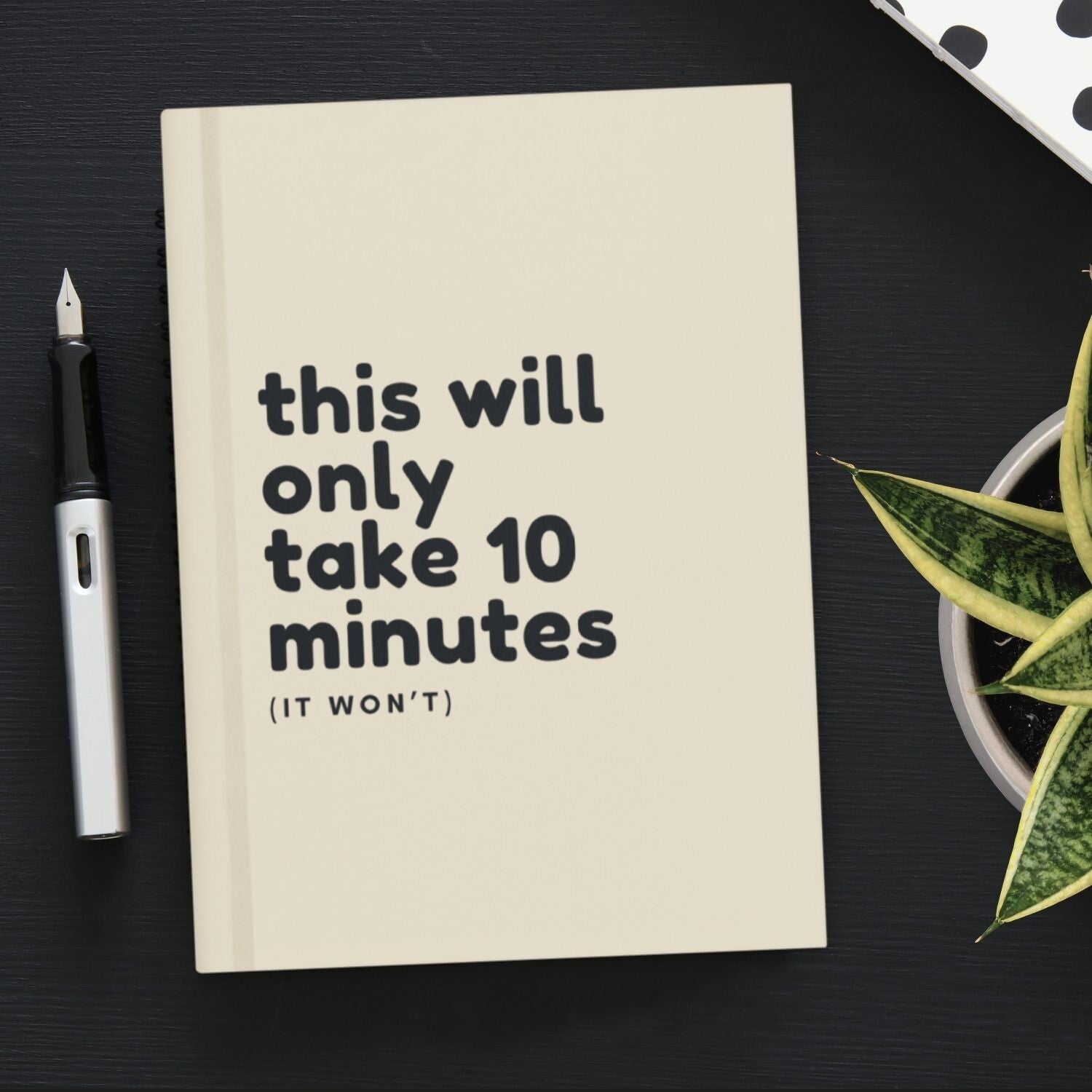 Beige hardcover lined journal titled This Will Only Take 10 Minutes. The journal is resting on a desk next to a pen.