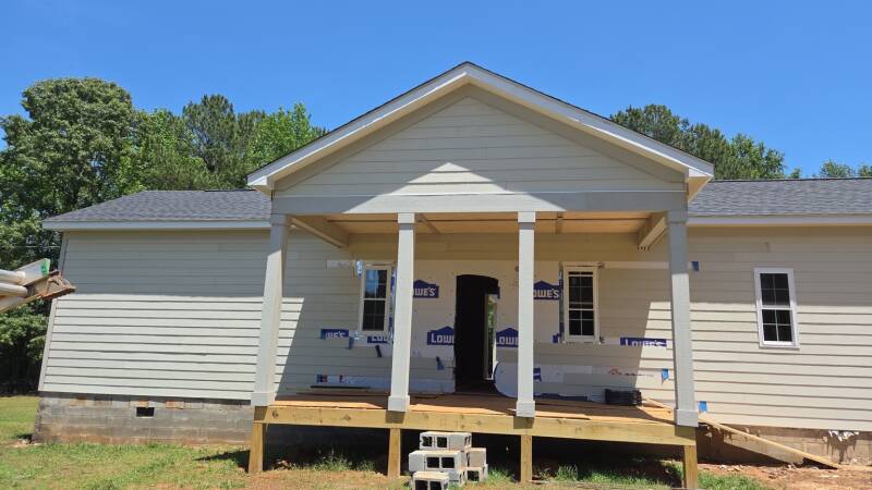 Front porch in progress: a gable entrance, wrapped columns and a raised wood platform create a welcoming focal point. / Porche frontal en proceso: entrada a dos aguas, columnas revestidas y plataforma de madera elevada.