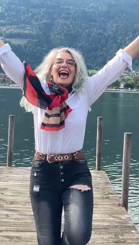 Frau am Strand mit weit geöffneten Armen im Sonnenaufgang, symbolisiert das Erwachen der Seele und innere Transformation