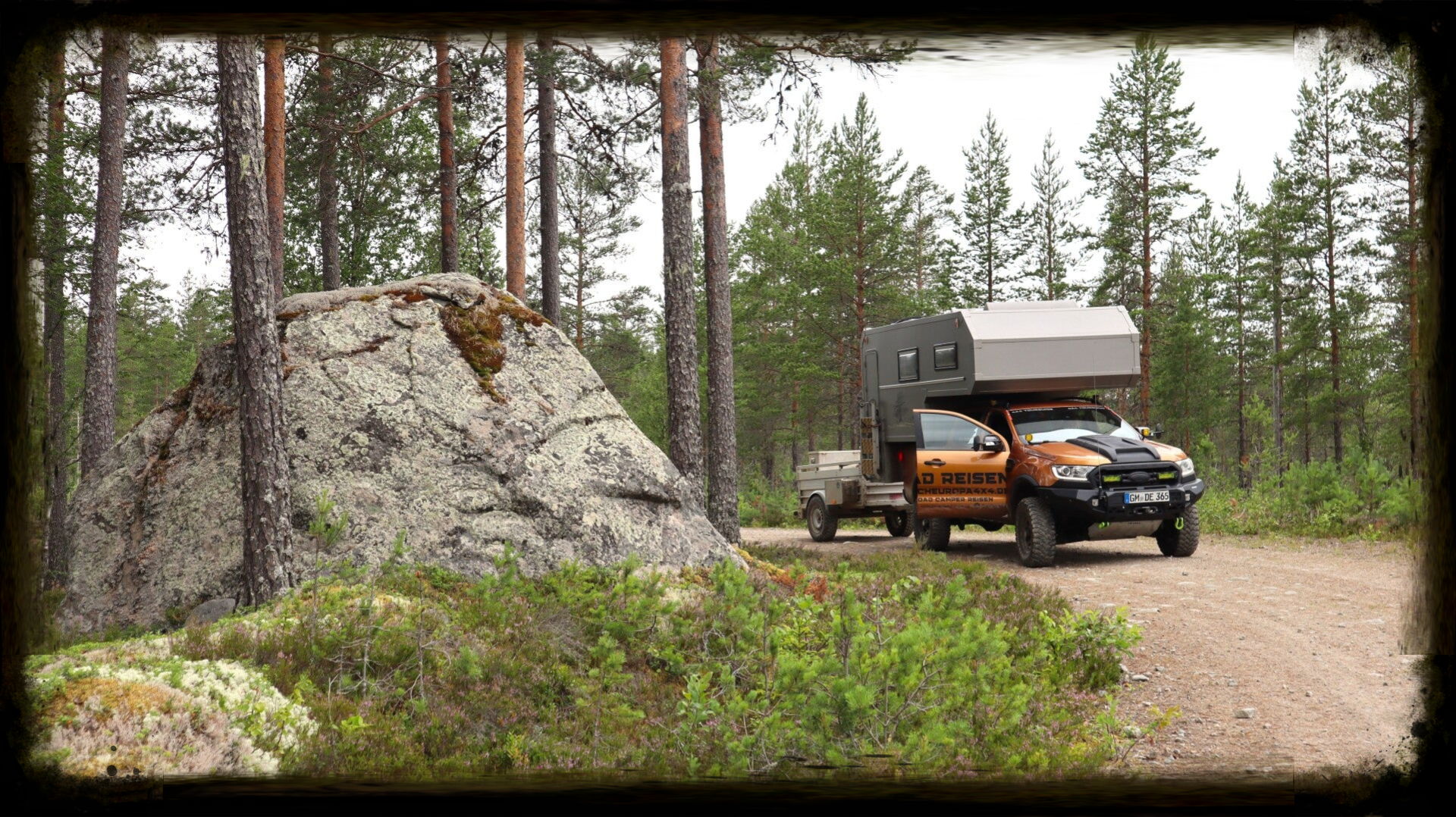 Offroad Camper auf Schotterpiste in Schweden neben großem Felsbrocken