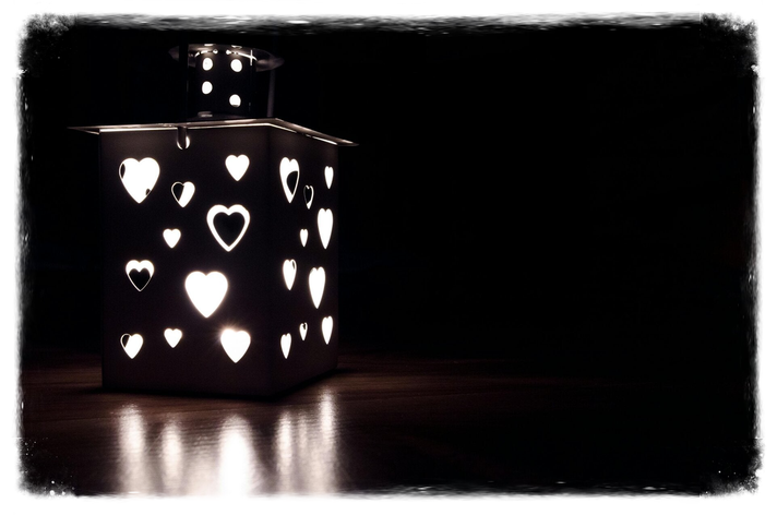 A lantern that is illuminated and the lights shooting through heart shapes in various sizes.