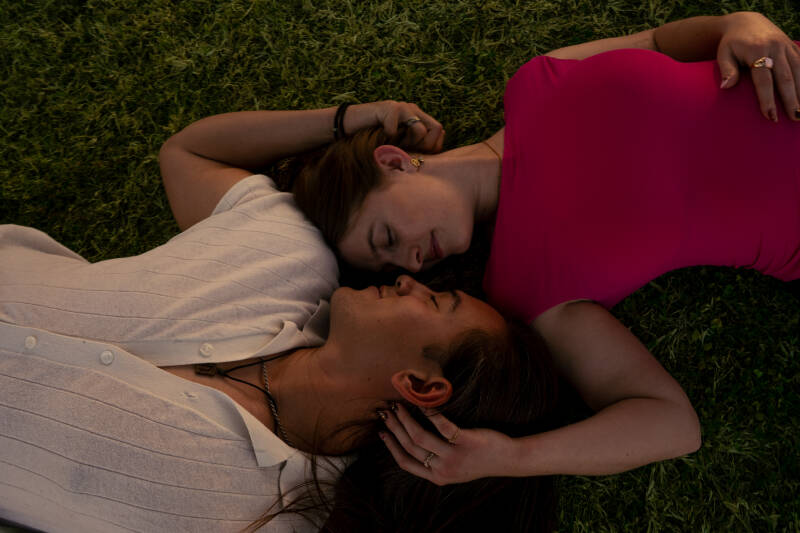 Couple lying down nose-to-nose in a field of grass. 