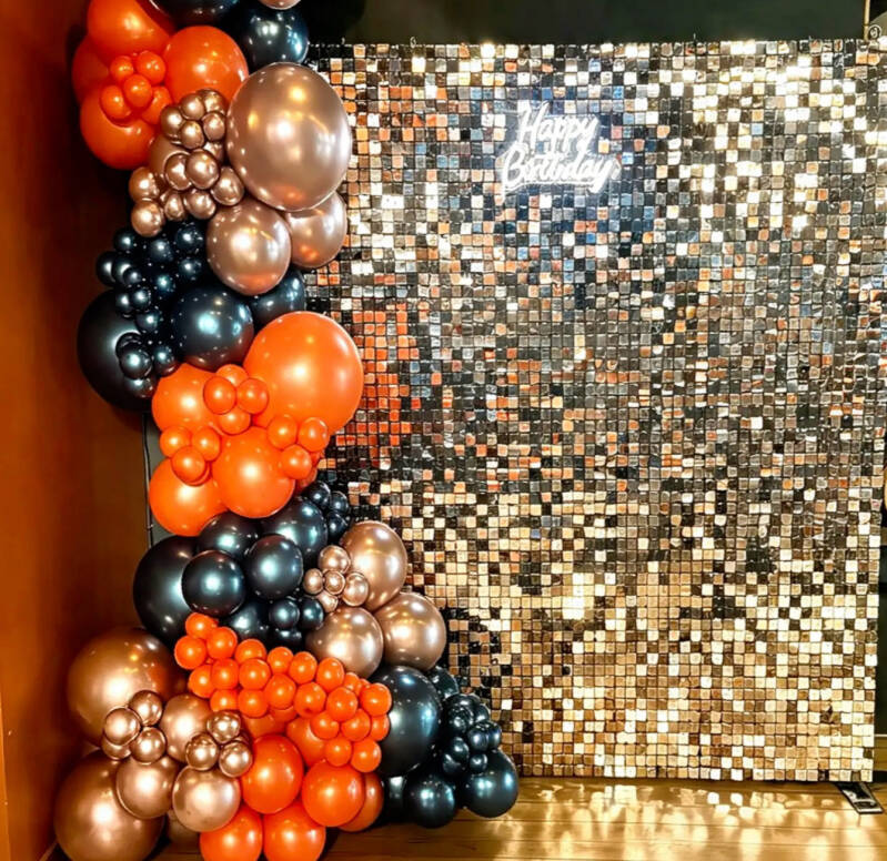 Bronze sequin shimmer wall with a Happy Birthday neon sign and orange, black and copper balloon garland