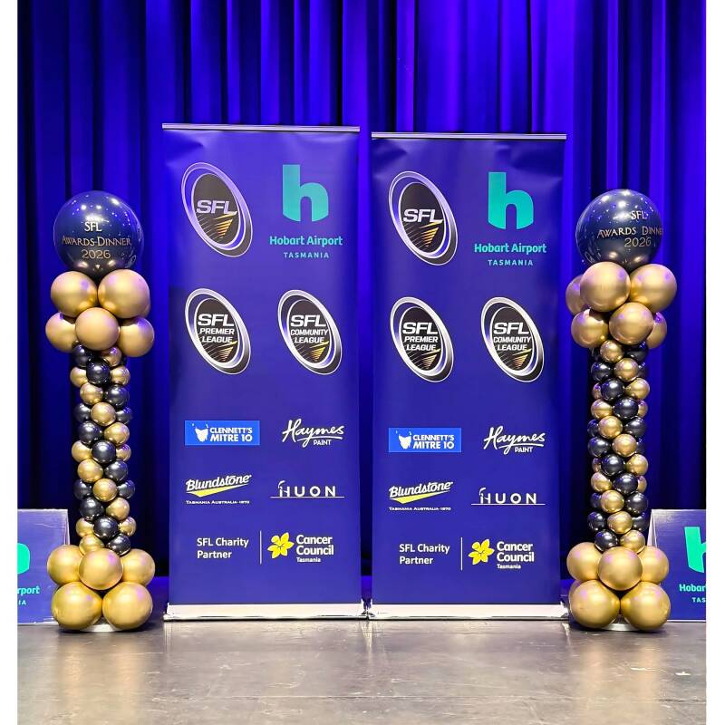 Navy, gold and silver balloon columns framing a branded step-and-repeat backdrop at a corporate event