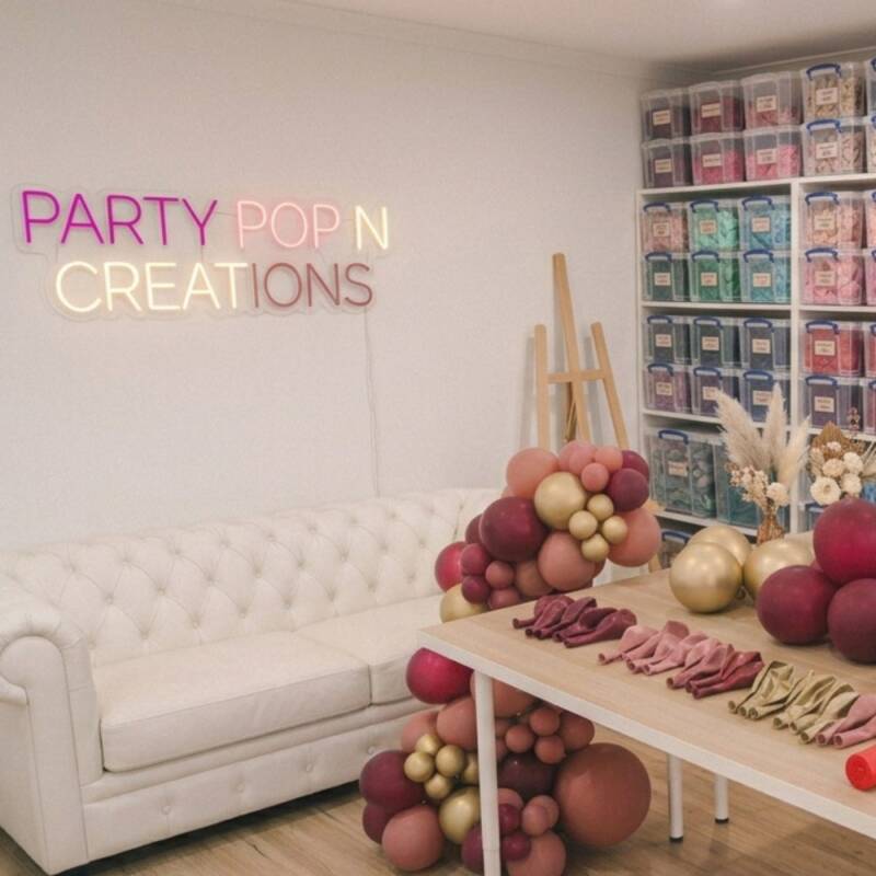 Party Pop 'N' Creations studio workshop with neon sign, balloon supplies and a garland being assembled