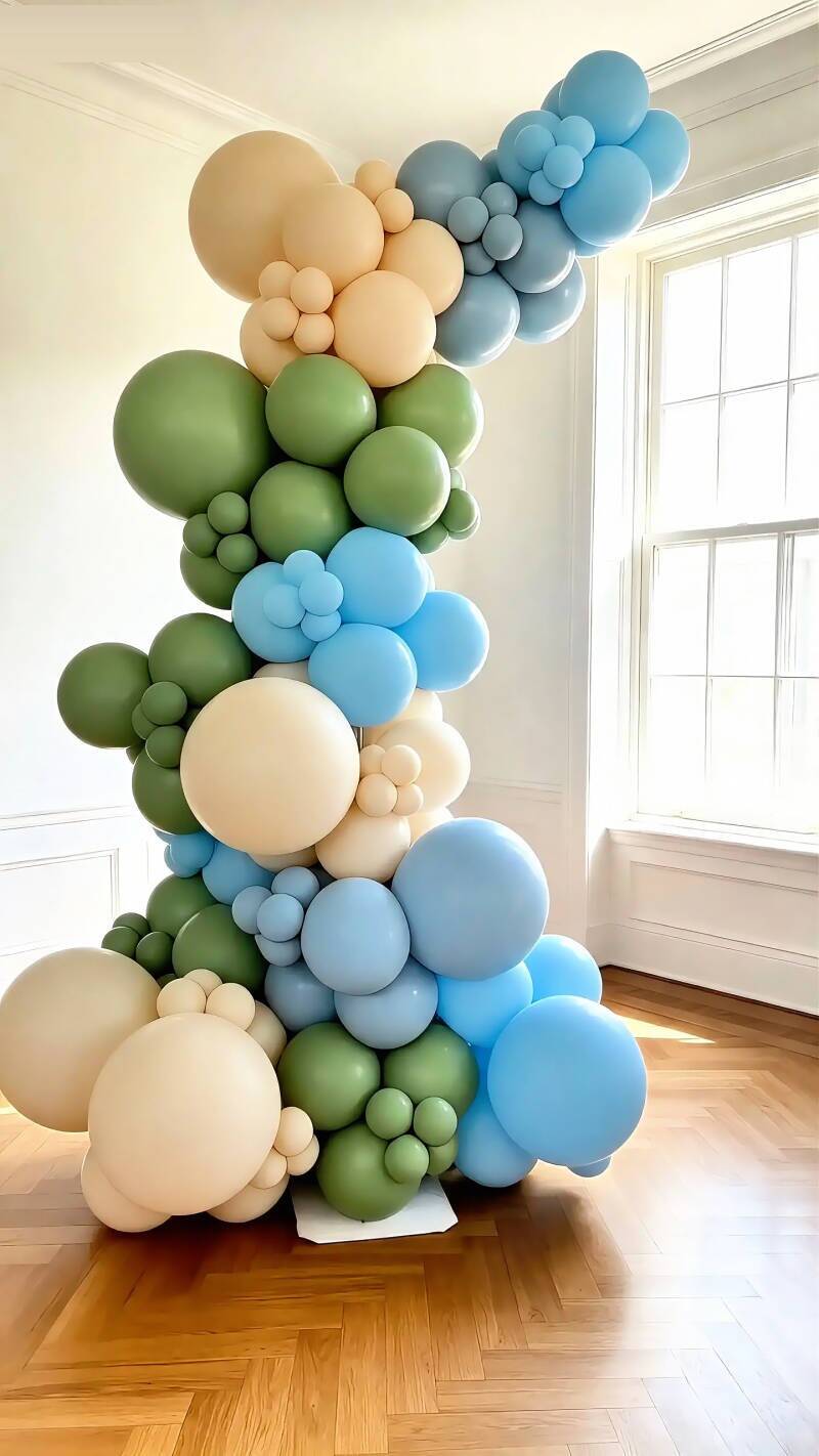 Tall organic balloon tower in sage green, sky blue and cream styled beside a window