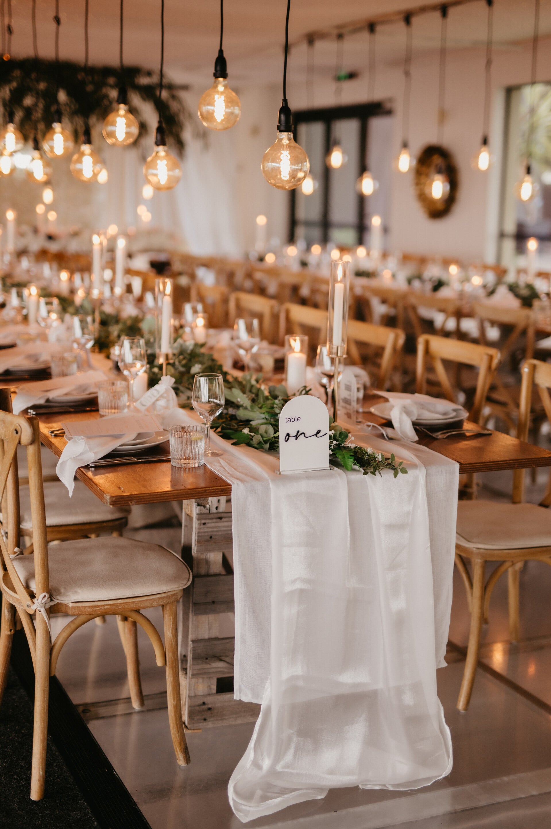Reception tables styled with greenery runners, candles and hanging edison bulb lights