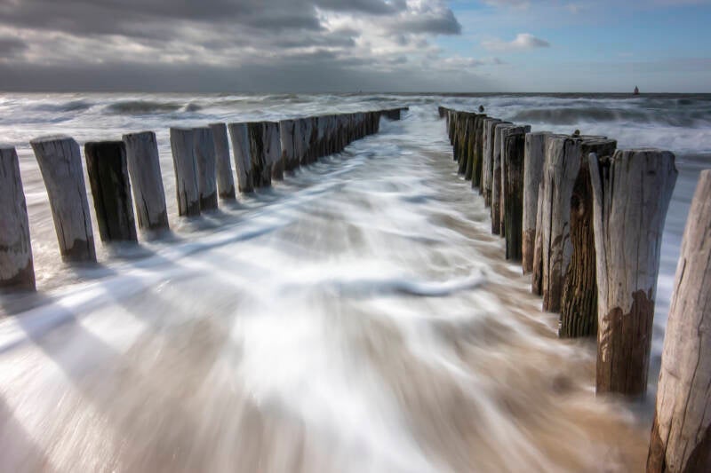 Hoge golven tussen paalhoofden strand Valkenisse