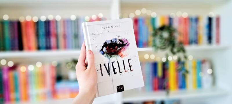 Een witte hand houdt 'Ivelle' van Laura Diane. Foto bij recensie door turnthepages.nl Rolstoelgebruiker en disabled bookstagrammer en blogger.